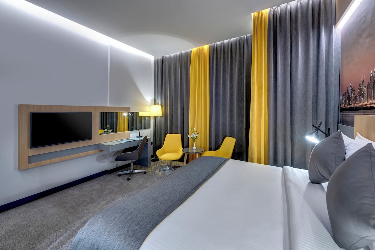 Ein Hotelzimmer mit einem großen Bett, einem Schreibtisch, einem Sessel, einem Fernseher und Vorhängen.