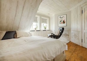 A bedroom with a large bed, a black chair, and a window with curtains.