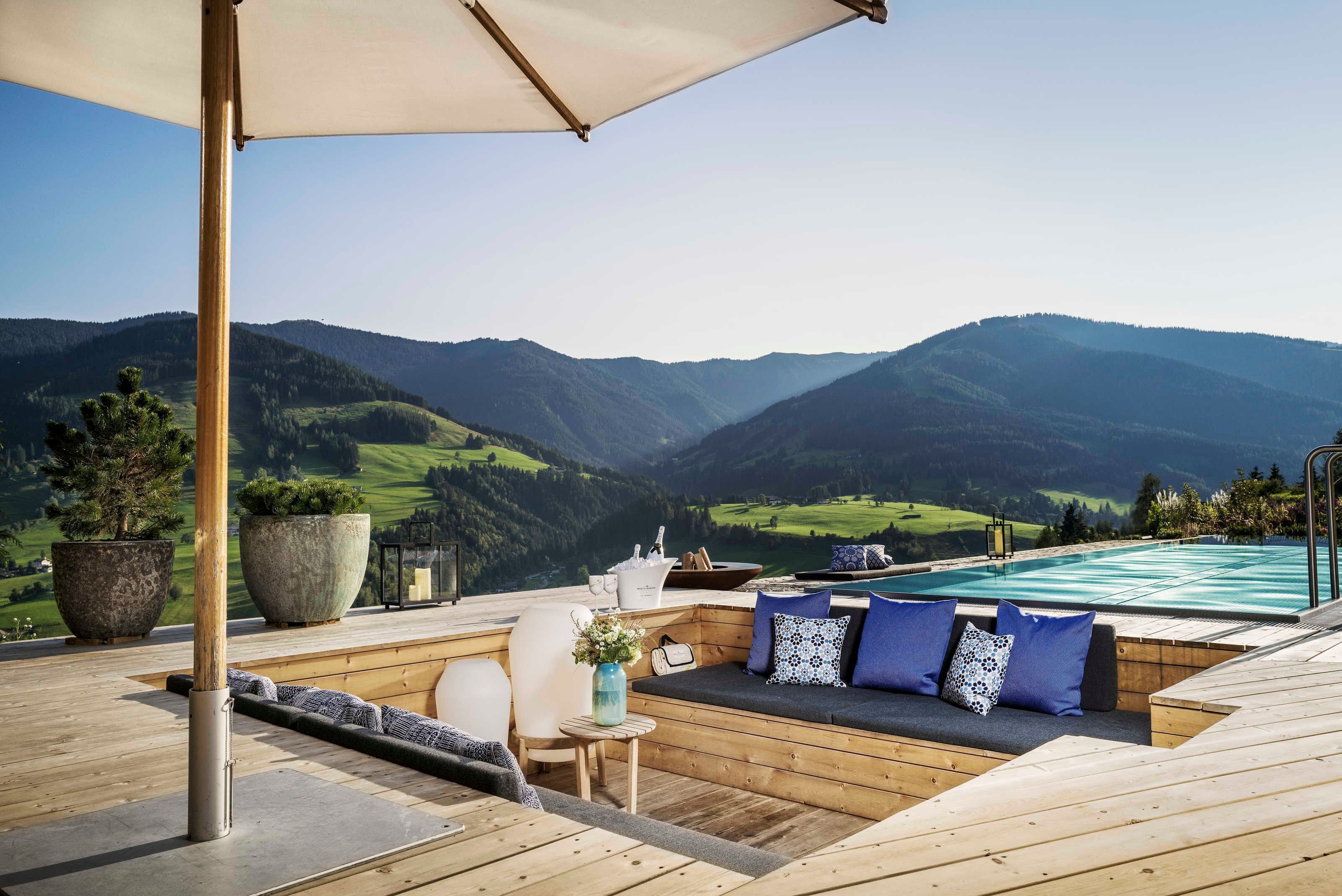 Una terraza de madera con piscina, zona de estar y plantas en macetas.
