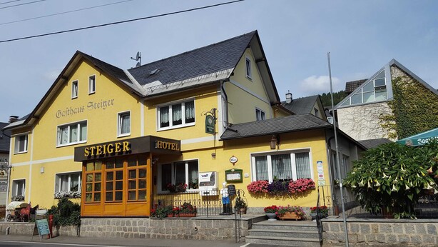 Un bâtiment à deux étages, doté d’une façade jaune, d’une enseigne indiquant « Hôtel Steiger » et d’un style architectural européen traditionnel.
