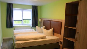 Une chambre à coucher avec un lit double, une tête de lit en bois, une fenêtre avec des rideaux et une armoire intégrée en bois.