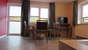 Ein Zimmer mit Holzboden, einem Fernsehgerät auf einem Schrank und einem Tisch mit Stühlen.