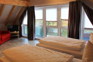 Una habitación con dos camas, un sofá rojo, un televisor y ventanas grandes con cortinas.