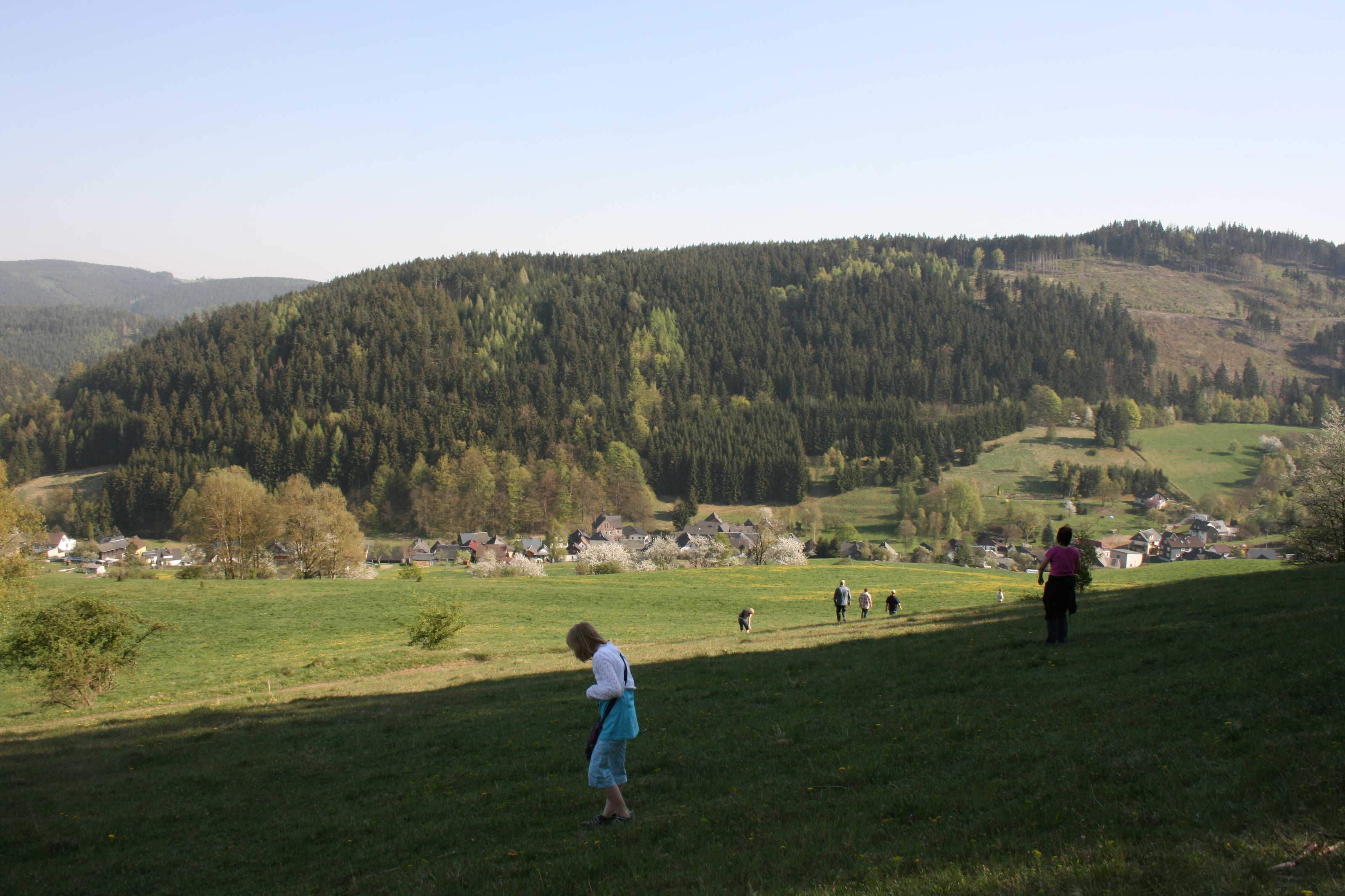 A rural landscape with a village in the valley, surrounded by hills and trees.