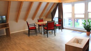 Un comedor con mesa y sillas de madera, una planta en maceta y vistas al exterior a través de amplios ventanales.