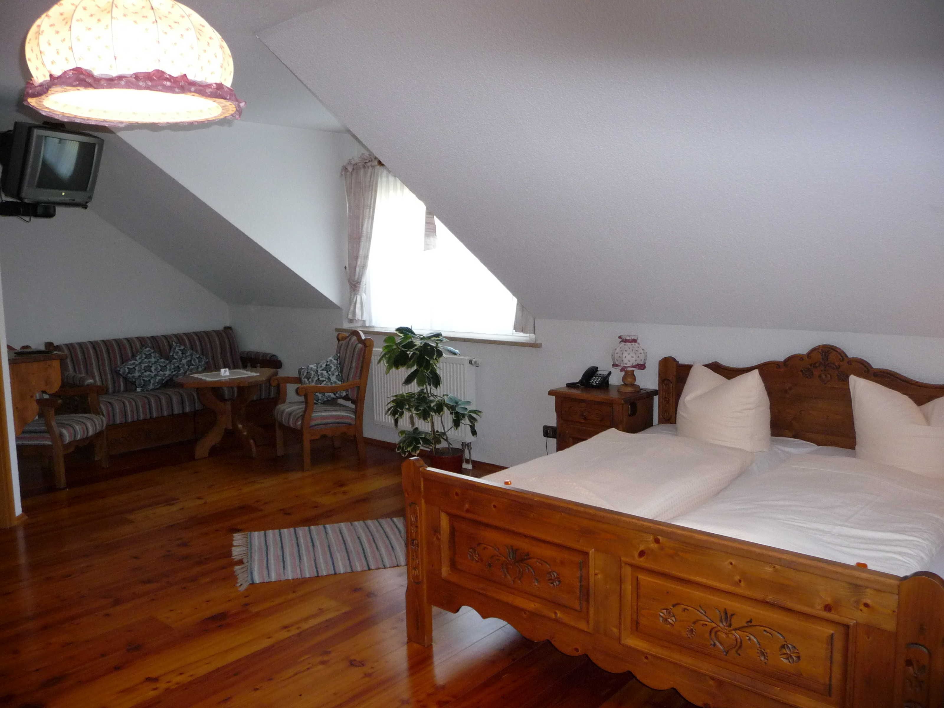 Une chambre à coucher avec un lit en bois, une petite table, une chaise, un téléviseur et une fenêtre avec des rideaux.