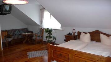 A bedroom with a wooden bed, a small table, a chair, a television, and a window with curtains.