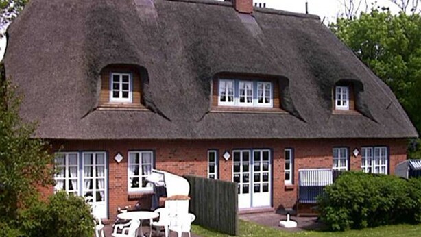 Een traditioneel rieten huis met een gevel van baksteen, meerdere ramen en een kleine tuin met terras.
