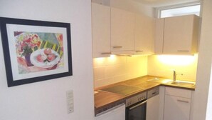 Een compacte keuken met witte kastjes, een vaatwasser, een oven en een spoelbak.