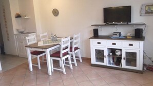 Een knus woongedeelte met een eettafel en stoelen, een kitchenette met een televisie en een klein kastje met glazen deuren.