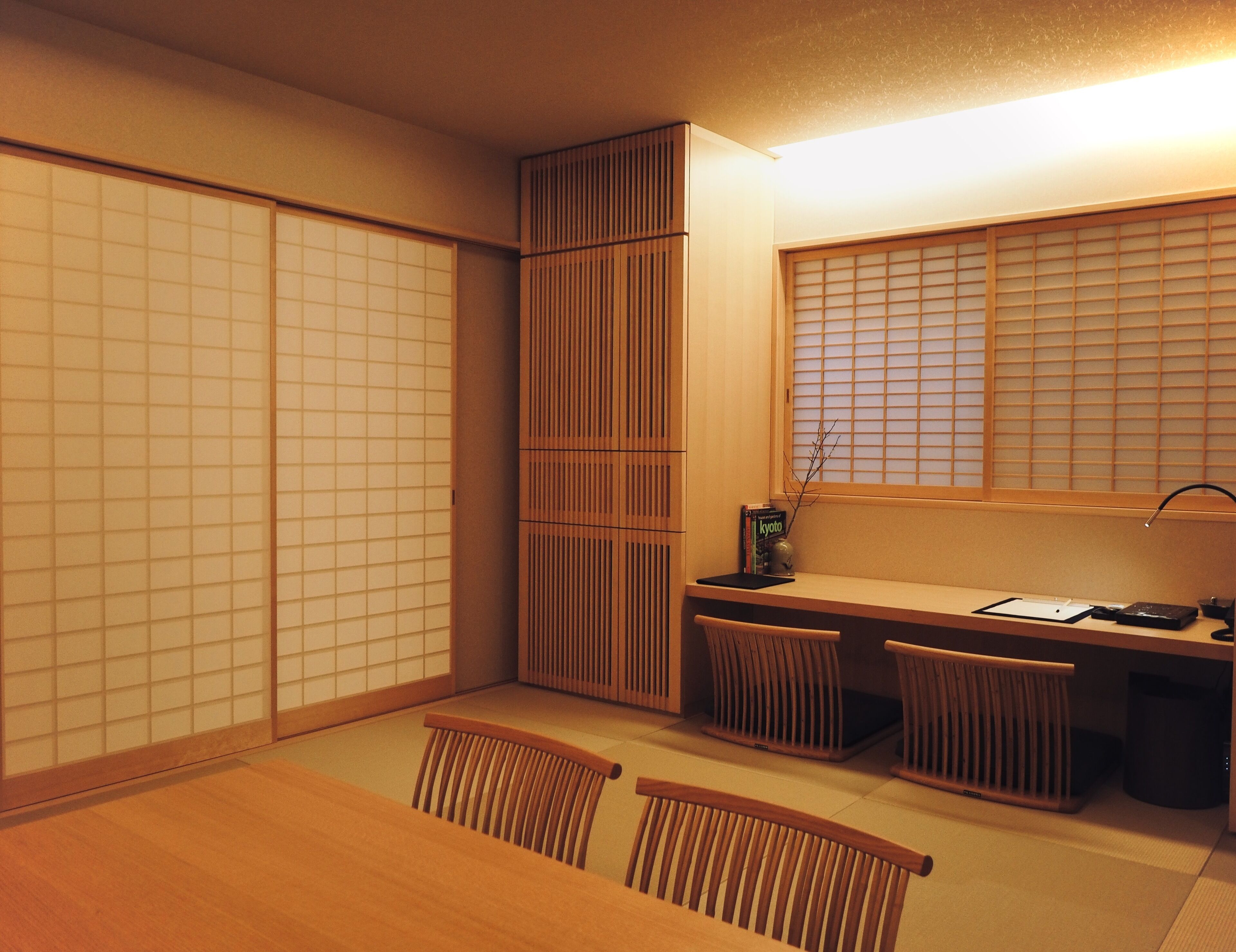 A traditional Japanese room with tatami flooring, sliding shoji doors, a low table with chairs, and a desk with a lamp and books.
