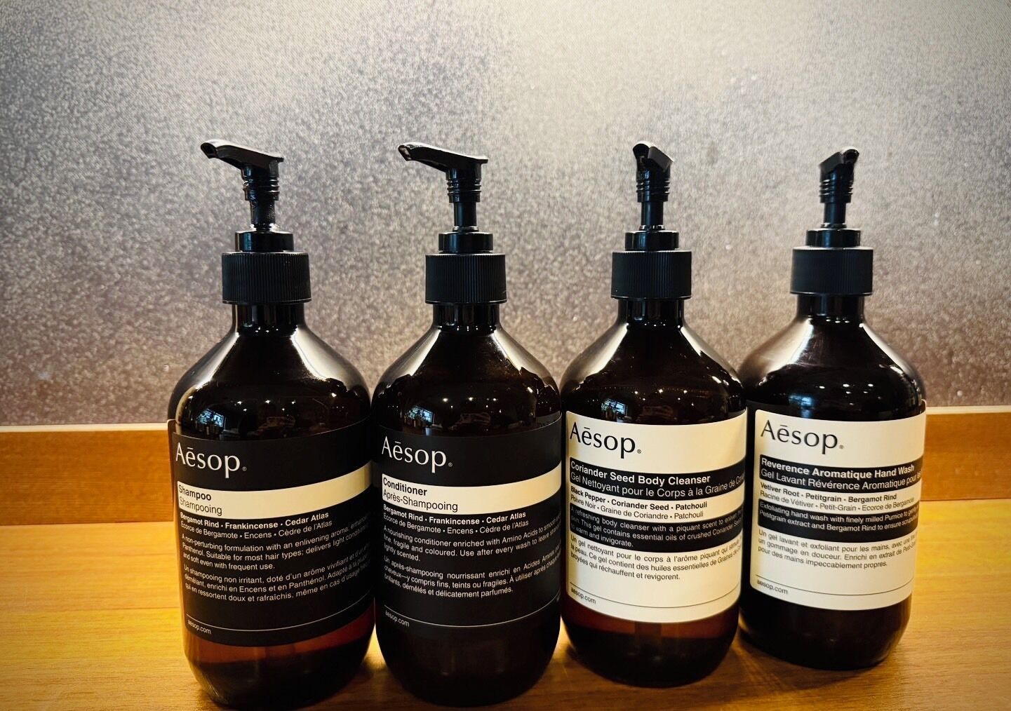 Four bottles of Aesop body care products on a wooden surface.