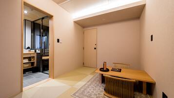 A modern, minimalist room with a wooden table and chairs, a small rug, and a sliding door leading to a kitchen area.