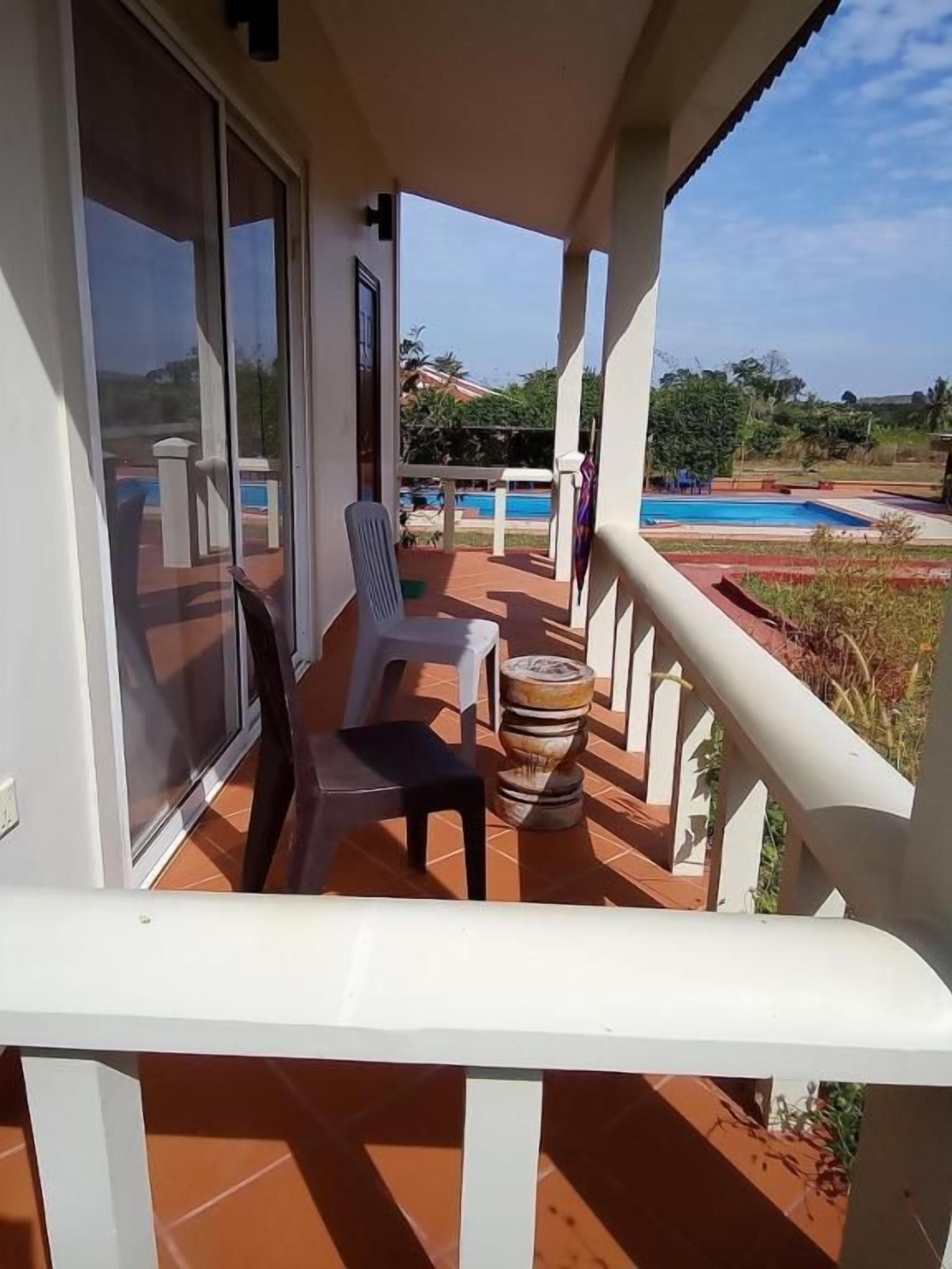 Un balcón con vista a una piscina, una silla y un taburete de madera decorativo.