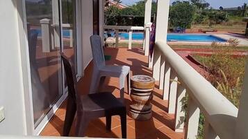 Un balcón con vista a una piscina, una silla y un taburete de madera decorativo.
