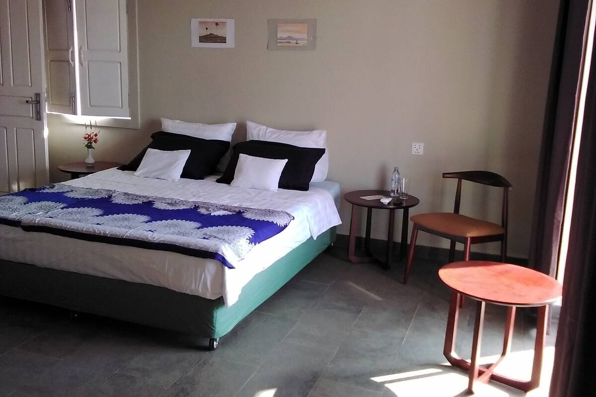 A bedroom with a bed, a small table, a chair, and a door.