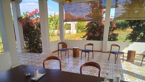 A covered outdoor dining area with a table and chairs, surrounded by a garden with various plants and flowers. - Koh Ker Hotel & Restaurant (Kuleaen)