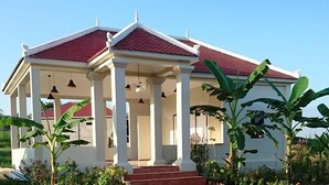 A two-story building with a red-tiled roof, white columns, and a covered porch. - Koh Ker Hotel & Restaurant (Kuleaen)