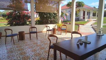 Uma área de pátio coberta com mesa e cadeiras, piso estampado e vista para uma casa e jardim.