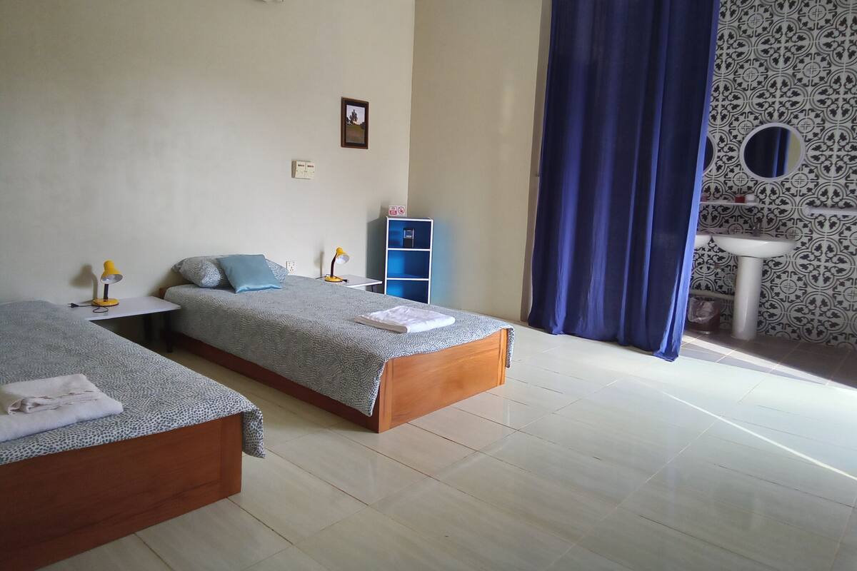 A bedroom with two beds, a desk, a wardrobe, and a bathroom with a sink and mirror.