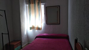 A small bedroom with a single bed, a window with curtains, a mirror on the wall, and a wooden chair. - Cozy and central bass (Ciudad Real)
