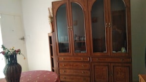 A wooden cabinet with multiple drawers and glass doors, a vase with flowers, and a red upholstered chair. - Cozy and central bass (Ciudad Real)