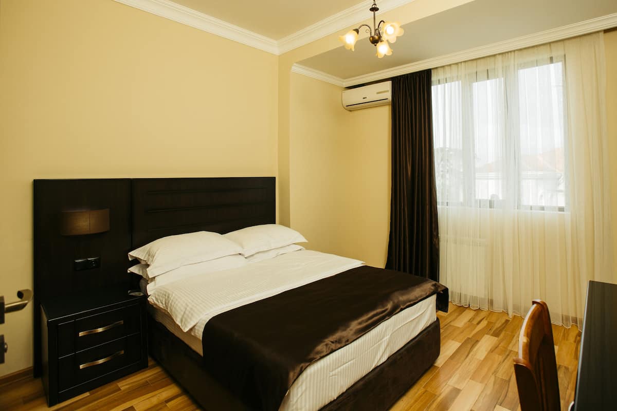 A hotel room with a bed, a desk, a chair, a lamp, and an air conditioning unit.