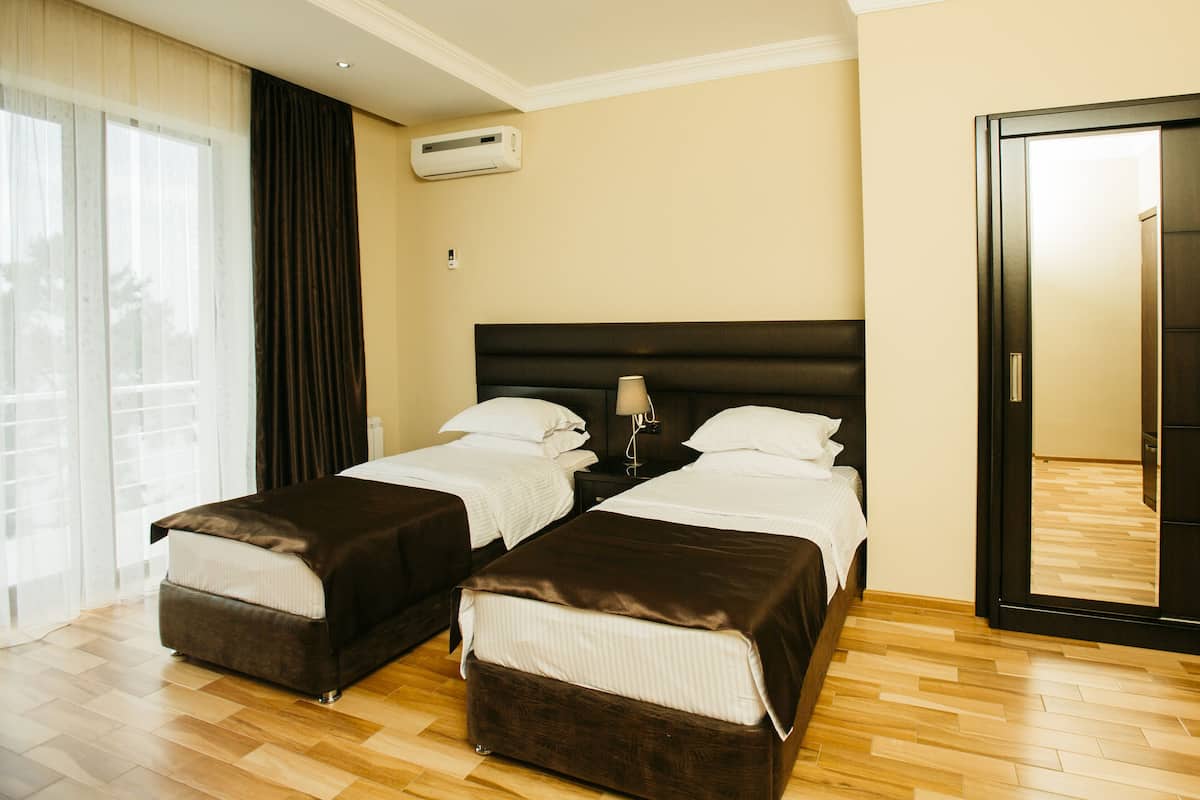 A hotel room with two beds, a wardrobe, a bedside table with a lamp, and an air conditioning unit.