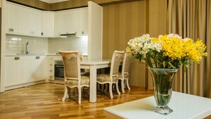 A modern kitchen with white cabinets, a dining table with four chairs, and a vase of yellow and white flowers on a white table. - Kobuleti Pearl Of Sea Hotel & Spa (Kobuleti)