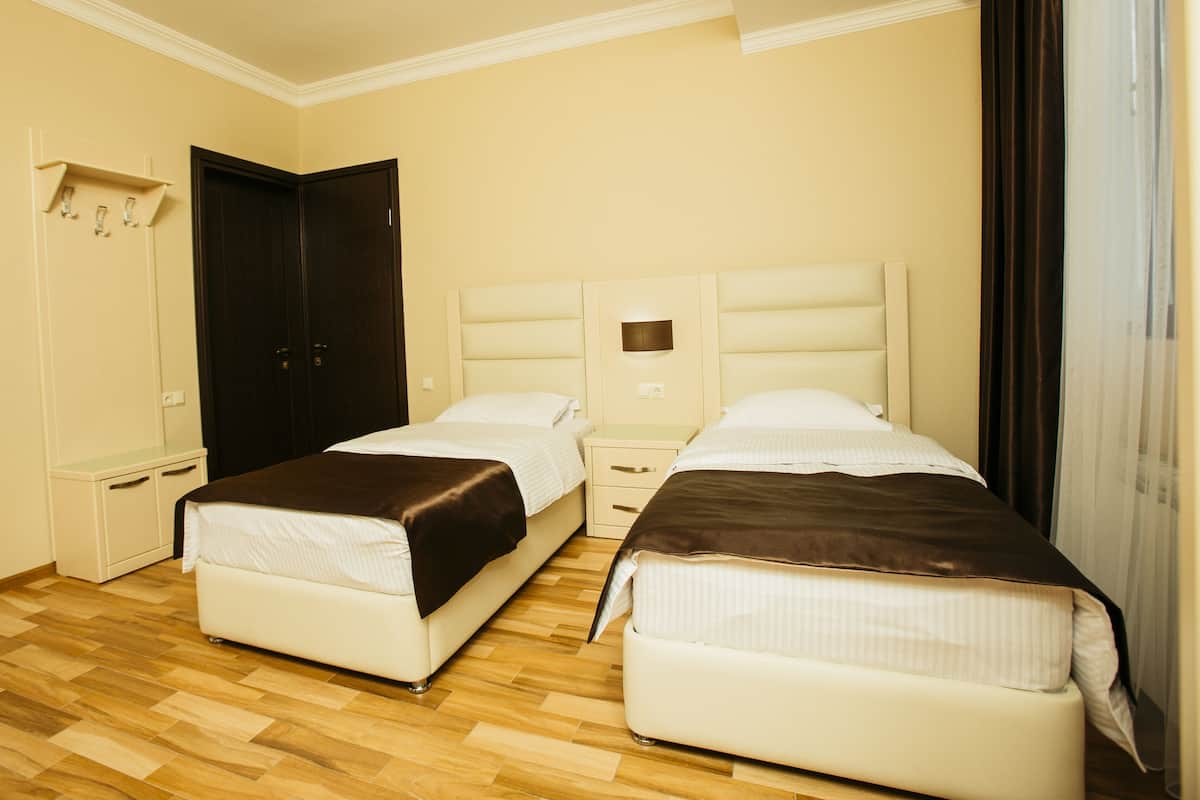 A hotel room with two beds, a wardrobe, and a small bedside table.