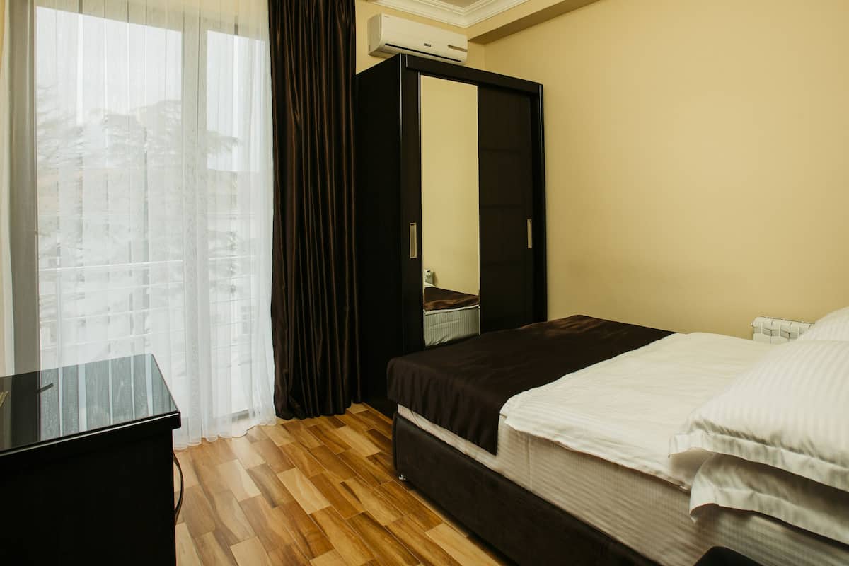 A hotel room with a bed, a mirror, a TV, and a window with curtains.