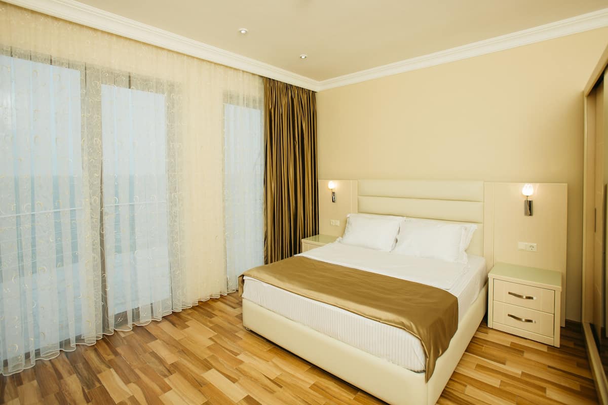 A hotel room with a large bed, wooden flooring, a nightstand, and a wall-mounted lamp.