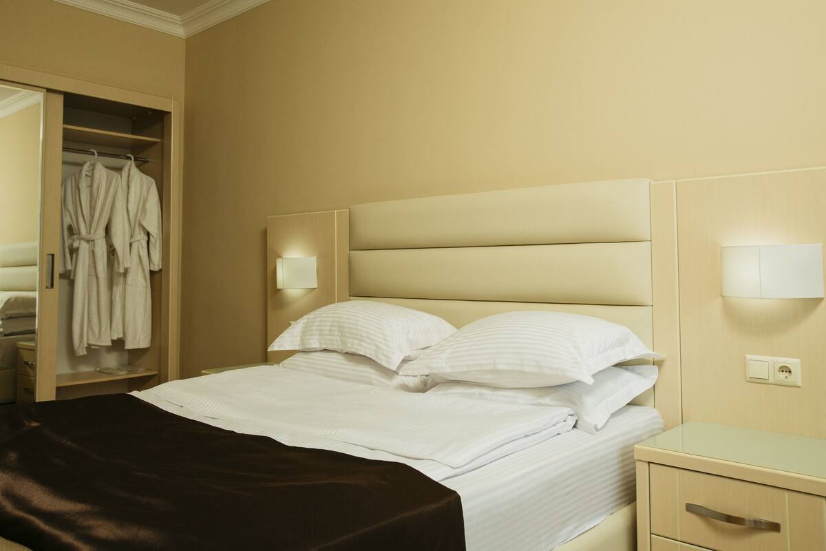 A hotel room with a bed, a nightstand, a bedside table, a wardrobe, and a mirror.