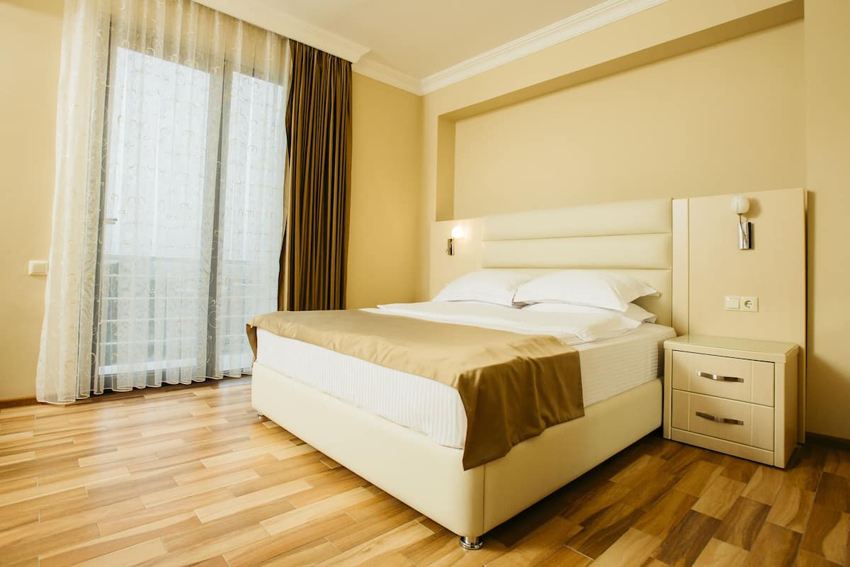 A hotel room with a bed, bedside tables, a nightstand, and a window with curtains.