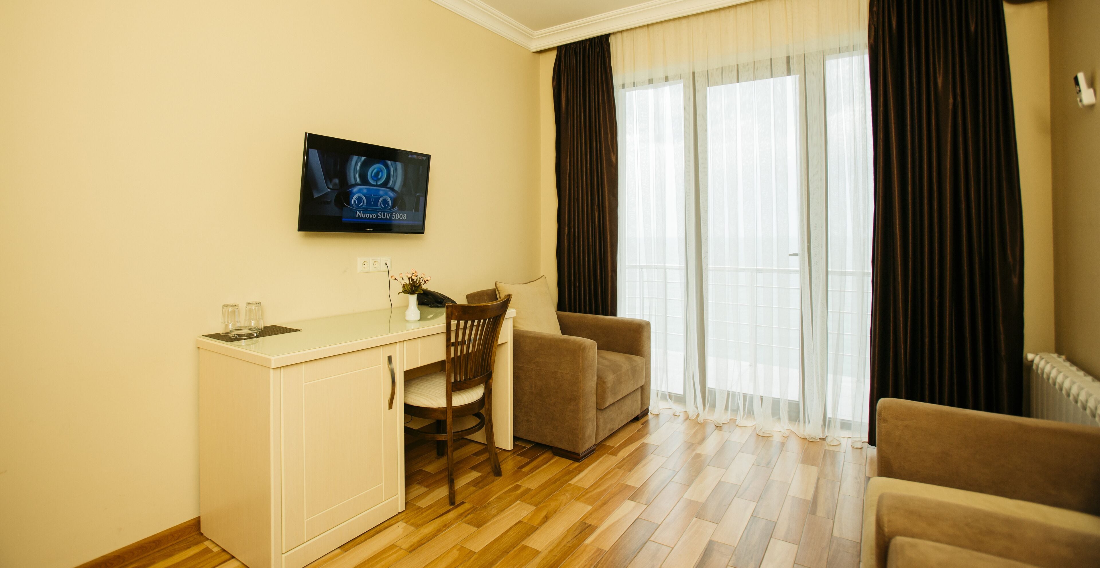 A hotel room with a kitchenette, a TV, a sofa, and a chair.