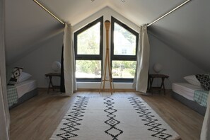 A room with a sloped ceiling, two beds, a standing lamp, and a large window with curtains.