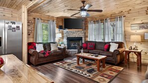 L’intérieur d’une cabane en rondins, avec une cheminée, deux canapés en cuir, une table basse en bois et un manteau de cheminée en pierre.