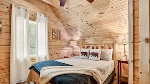 Une chambre confortable dans un chalet en rondins, avec un lit, des rideaux, une lampe et un mur décoré de motifs animaliers.
