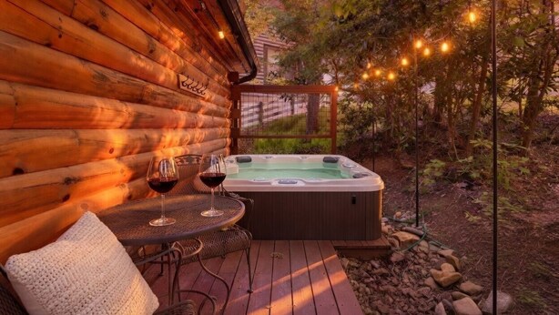 Une cabane en bois avec un bain à remous, une table avec deux verres à vin et un coin salon confortable.
