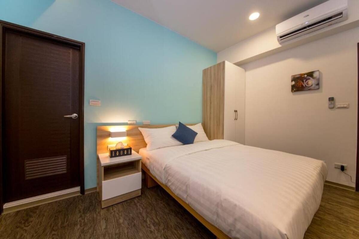 A bedroom with a bed, bedside table, nightstand, wardrobe, and an air conditioning unit.