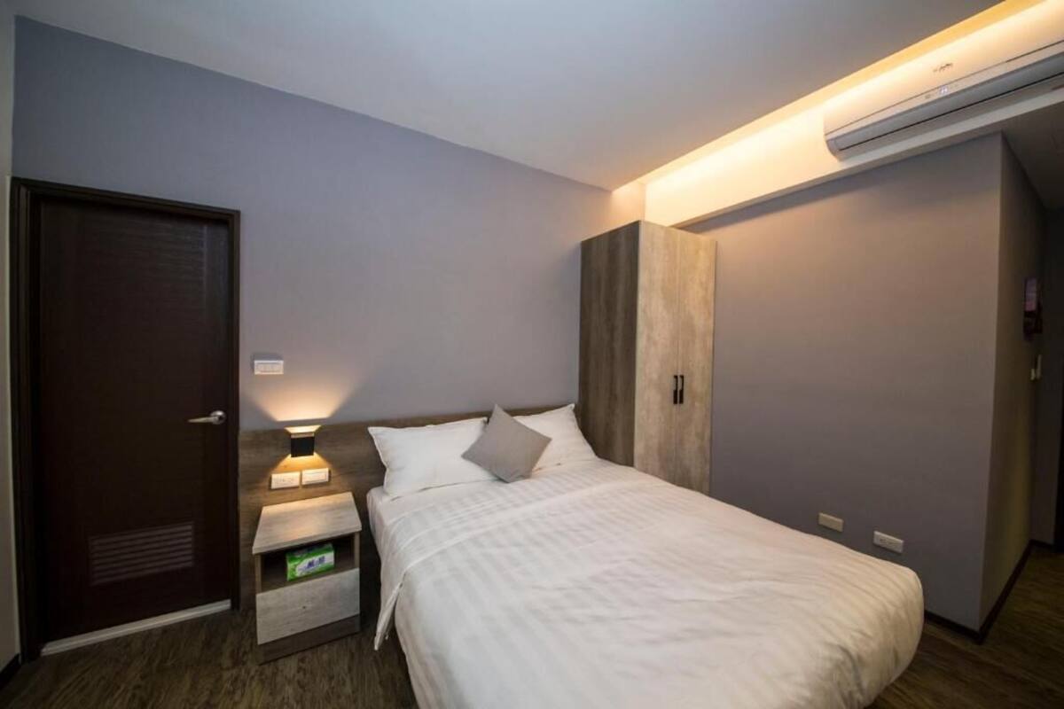 A modern hotel room with a bed, bedside table, and a wardrobe.
