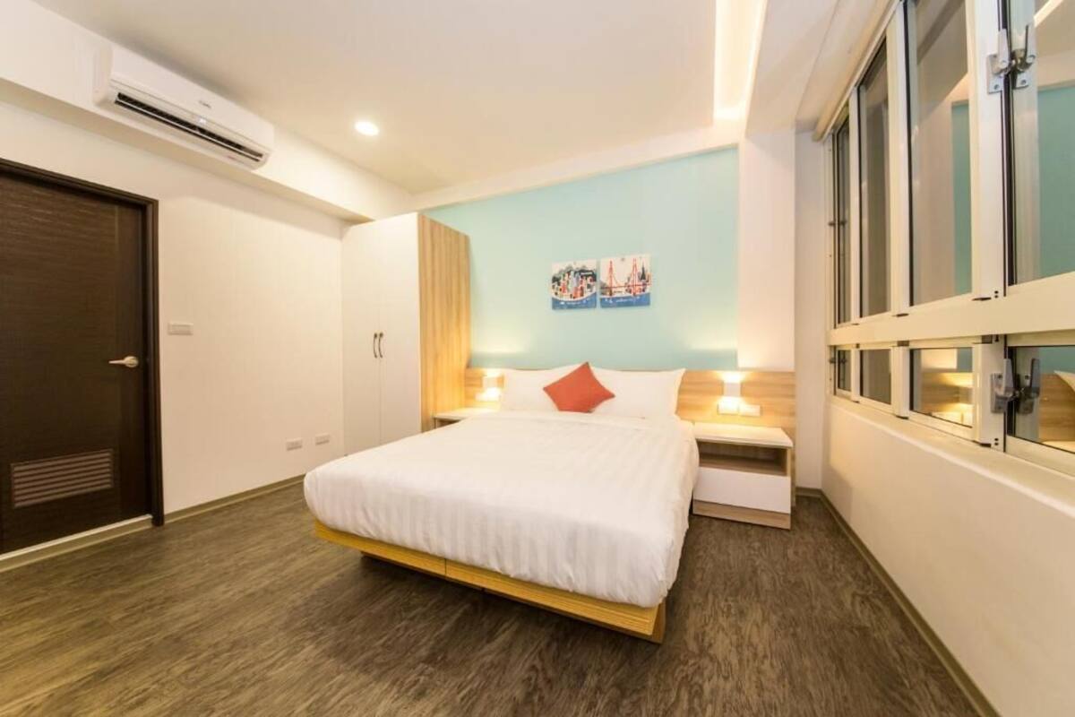 A modern hotel room with a bed, bedside tables, and a large window.