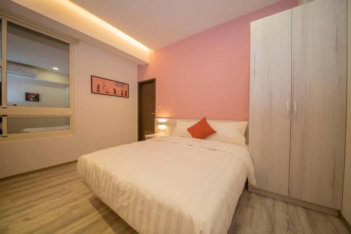 A bedroom with a bed, a wardrobe, a nightstand, a window, and a wall-mounted picture.