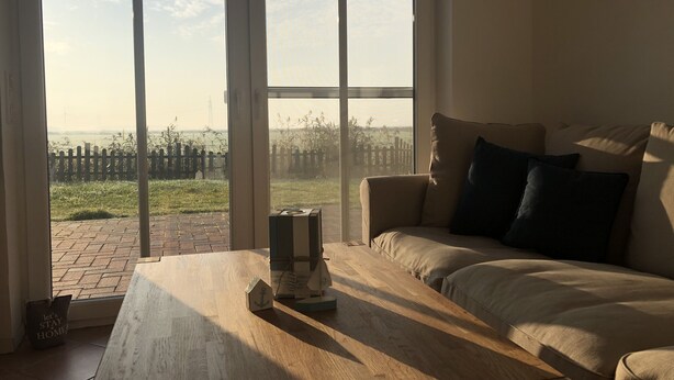 A room with a large window, a wooden table, and a sofa with cushions. - North Sea vacation with children (Dornum)