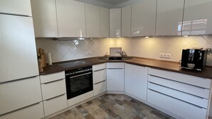 A modern kitchen with white cabinets, a built-in oven, a coffee machine, and a tiled backsplash. - North Sea vacation with children (Dornum)