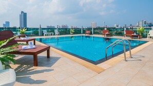 Piscina no terraço com espreguiçadeiras e vista para o horizonte da cidade.