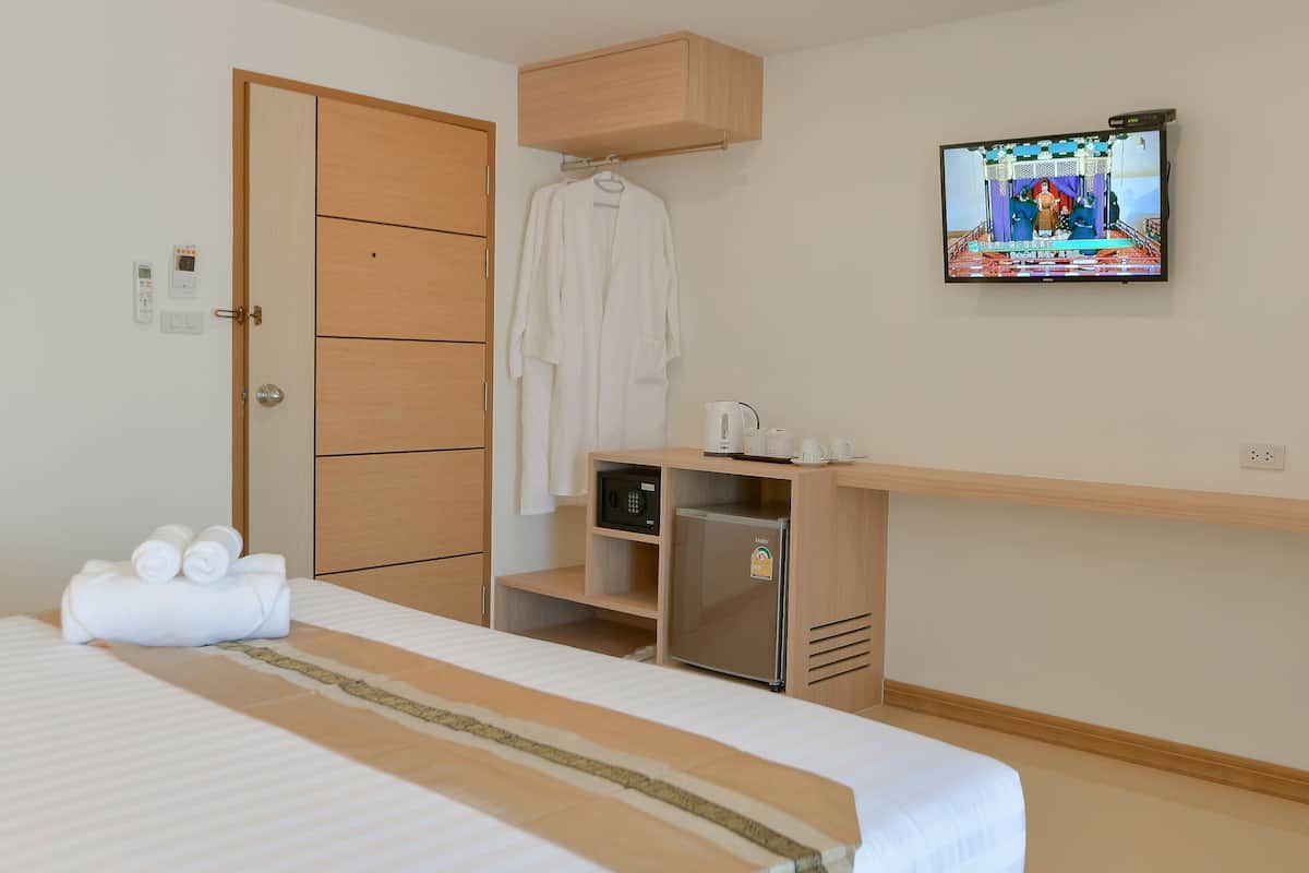 A hotel room with a bed, a TV mounted on the wall, a wooden wardrobe, a minibar, and a towel on the bed.