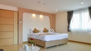 Quarto de hotel moderno com uma cama grande, uma mesinha redonda e um armário de madeira com um vaso de flores.