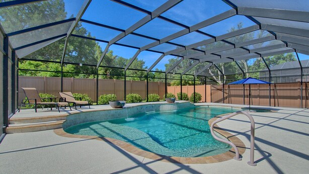 Piscina exterior techada con una característica de agua azul cristalina, rodeada por una estructura metálica y una valla de madera.