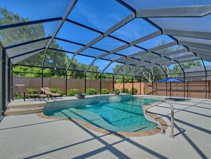 Une piscine extérieure couverte, avec un bassin aux eaux d’un bleu limpide, entourée d’une structure métallique et d’une clôture en bois.
